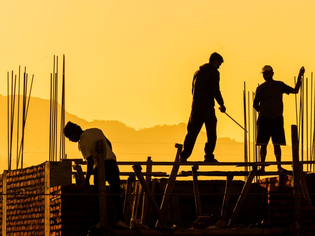 pexels-photo-13319079-13319079 Silhouetted workers on a construction site at sunset, highlighting the manual labor involved.
