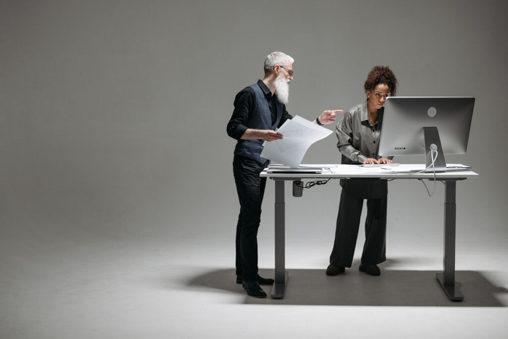 pexels-photo-8000551-8000551 A senior man and a woman working together at a desk in a modern office setting, focusing on a project.
